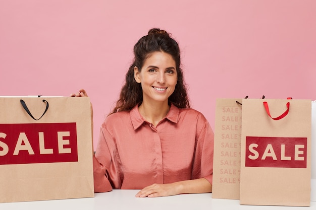 Portret pięknej kobiety z kręconymi włosami, uśmiechając się do kamery, siedząc przy stole z torby na zakupy