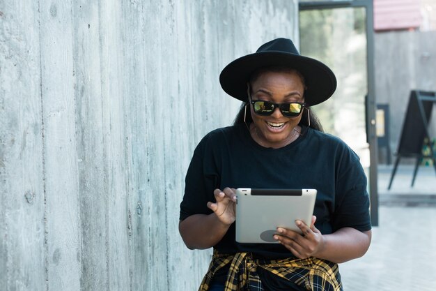 Portret pięknej kręconej Afroamerykanki stojącej w tle miejskim i trzymającej cyfrową tabletkę urocza młoda kobieta z komputerem typu tablet