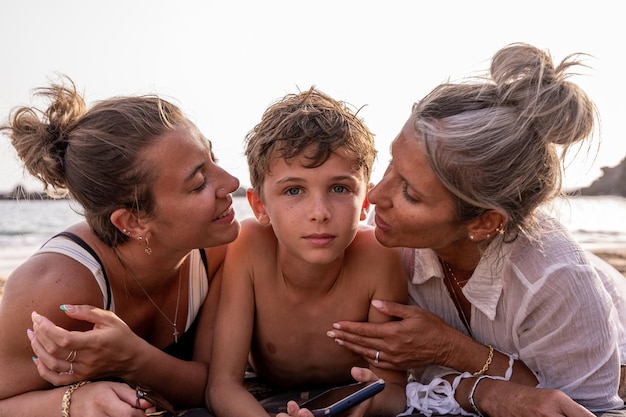 Portret pięknej matki w średnim wieku i jej córki całującej najmłodsze dziecko na plaży