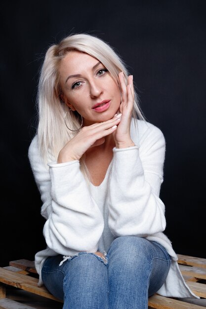 Zdjęcie portret pięknej młodej atrakcyjnej kobiety w białym swetrze z niebieskimi oczami i długimi blond włosami.
