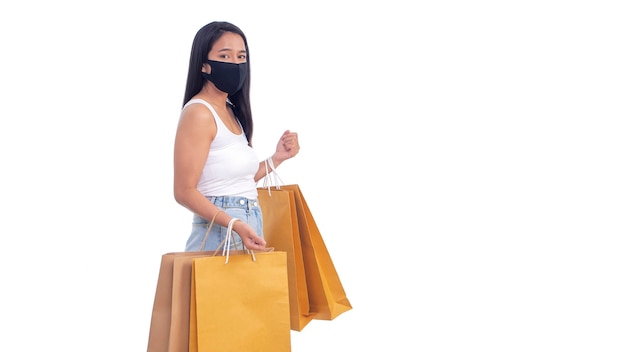 Portret pięknej młodej azjatyckiej kobiety noszącej maskę ochronną i trzymającej torby na zakupy na białym tle