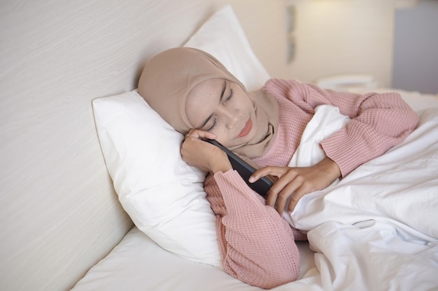 Portret pięknej młodej azjatyckiej muzułmanki w chustce na głowie leżącej w łóżku i śpiącej