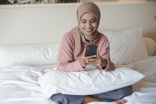 Portret pięknej młodej azjatyckiej muzułmanki w chustce na głowie podczas korzystania ze smartfona