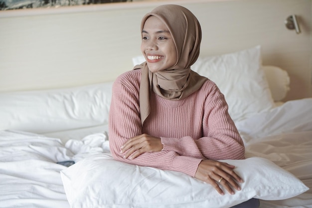 Portret pięknej młodej azjatyckiej muzułmanki w chustce na łóżku na wakacjach w hotelu