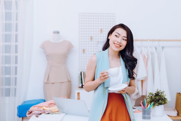 Portret pięknej młodej bizneswoman azjatyckiej projektantki mody w jej studio podczas picia kawy