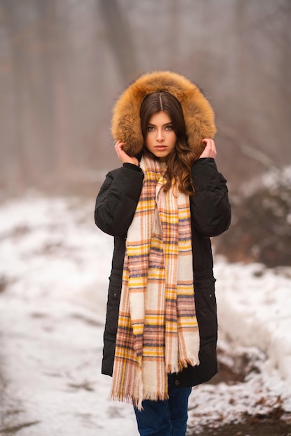 Zdjęcie portret pięknej młodej brunetki w zimowym płaszczu z futrzanym kapturem i ciepłym szalikiem.