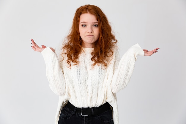 Portret pięknej młodej dziewczyny redheaded stojącej na białym tle na białym tle, wzruszając ramionami