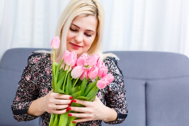 Portret pięknej młodej dziewczyny w sukni trzymającej duży bukiet tulipanów w domu na kanapie