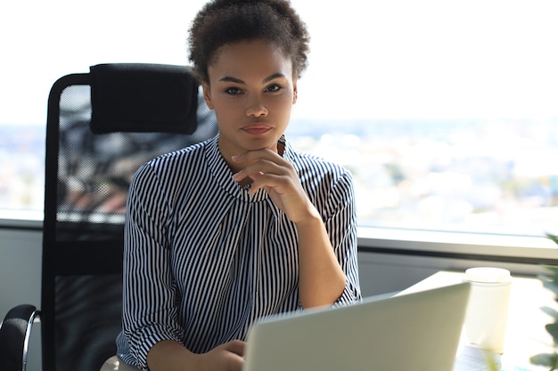 Portret pięknej młodej kobiety african american pracy z laptopem siedząc przy stole.