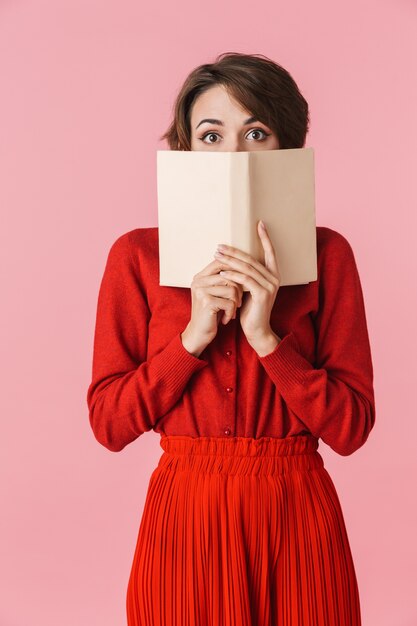 Portret pięknej młodej kobiety na sobie czerwone ubrania stojącej na białym tle, trzymając otwartą książkę