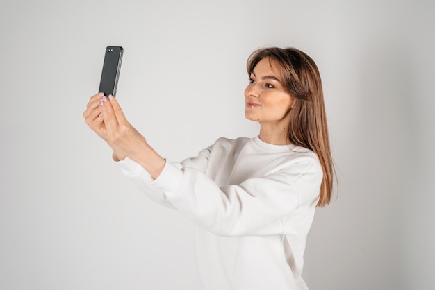 Zdjęcie portret pięknej młodej kobiety podczas robienia selfie i stojąc na białym tle