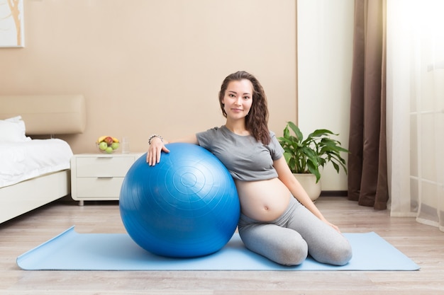 Portret pięknej młodej kobiety w ciąży ćwiczenia z niebieskim fitball w pokoju domowym. Wypracowanie i fitness, koncepcja ciąży.