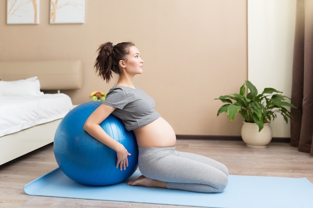 Portret pięknej młodej kobiety w ciąży ćwiczy z niebieskim fitballem w pokoju domowym