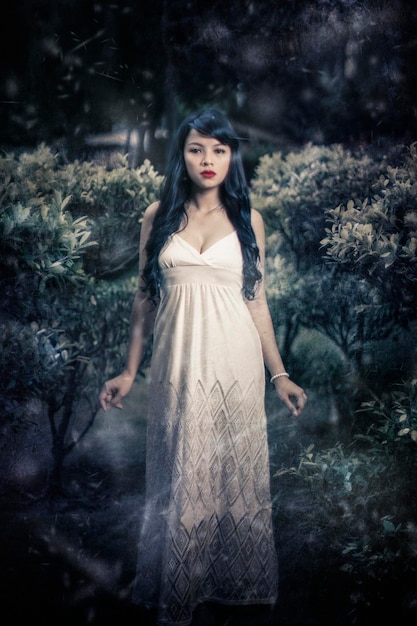 Portret pięknej młodej kobiety w sukience stojącej pośród roślin w lesie