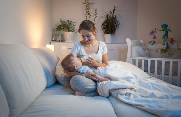 Portret pięknej młodej matki, dając mleko do swojego chłopca w łóżku w nocy. Koncepcja rodzicielska