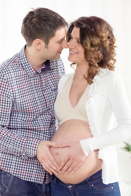 Portret pięknej młodej pary tworzącej kształt serca na brzuchu kobiety w ciąży.