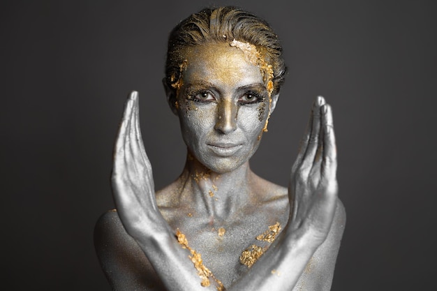 Portret pięknej modelki ze złotą i srebrną farbą na skórze i włosach w studio