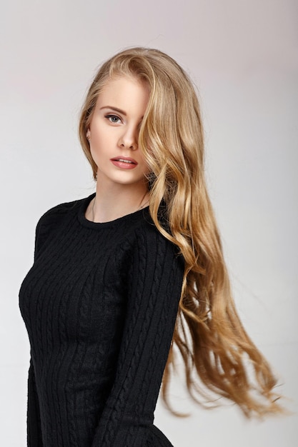 Portret pięknej mody blond modelki w czarnej sukience na szarym tle