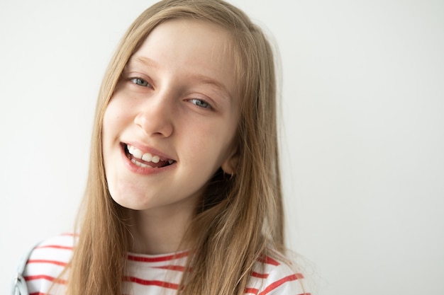 Portret pięknej nastolatka z długimi włosami uśmiechający się stojący na białej ścianie.