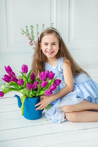 Portret pięknej niebieskookiej dziewczynki z bukietem tulipanów w jasnym pokoju