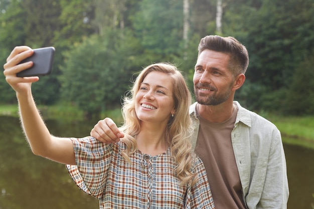 Portret Pięknej Pary Dla Dorosłych, Biorąc Selfie, Pozowanie Nad Jeziorem W Zielonej Scenerii Wsi