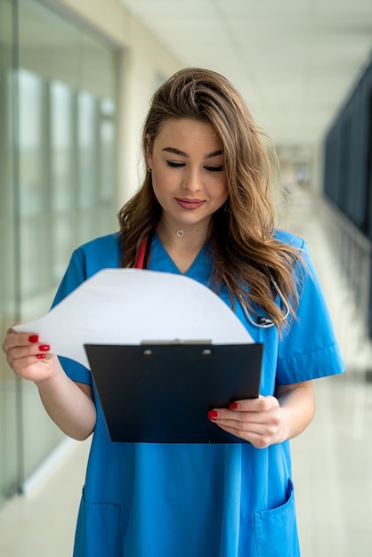 Zdjęcie portret pięknej pielęgniarki w niebieskim mundurze ze schowka w nowoczesnym szpitalu. pojęcie medyczne