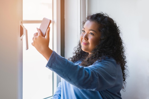 Portret pięknej pulchnej młodej kobiety Łacińskiej biorącej selfie z telefonem komórkowym w pomieszczeniu