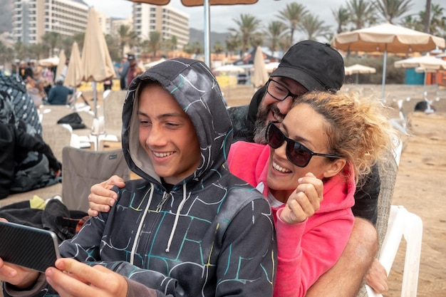 Portret pięknej rodziny siedzącej razem na plaży matka ojciec i syn patrząc na telefon