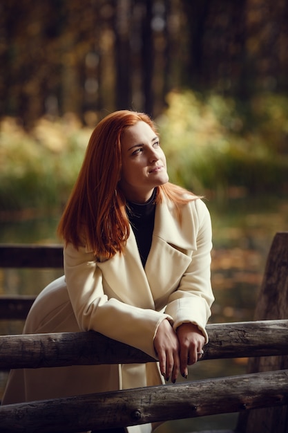 Portret pięknej, rozmarzonej i smutnej dziewczyny z czerwonymi włosami w białym fartuchu jesienią