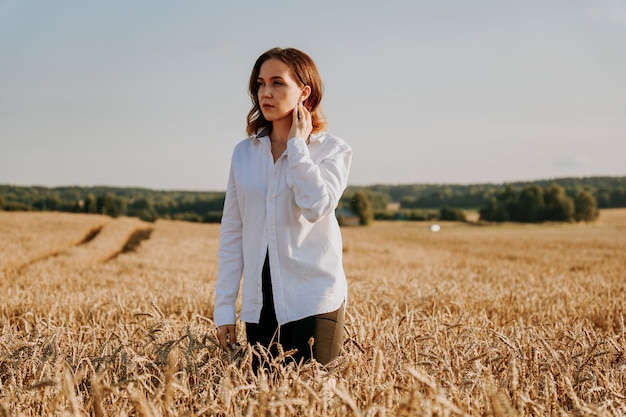 Portret pięknej rudowłosej dziewczyny w białej koszuli. Stoi na polu żyta w słoneczny dzień. Spokojny wyraz twarzy. Pojęcie ustępstw