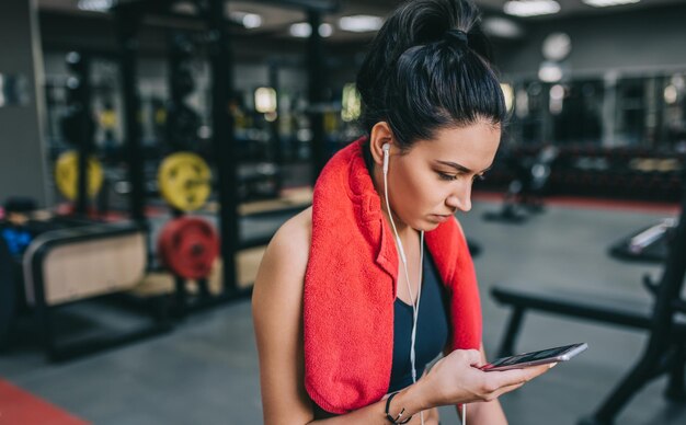 Portret pięknej, sportowej młodej kobiety słuchającej muzyki ze swojego smartfona, przygotowującej się do ciężkiego treningu na siłowni Ludzie technologia fitness i koncepcja sportu