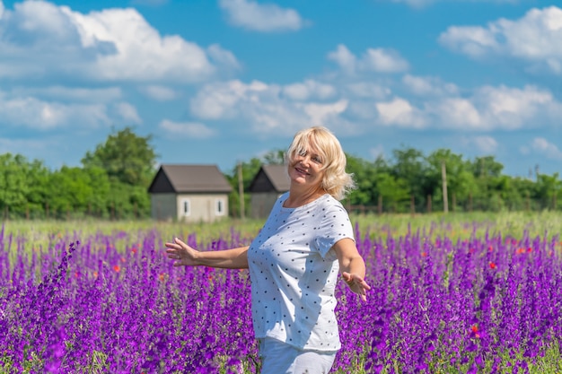 Portret pięknej szczęśliwej blondynki w średnim wieku na polu z kwiatami w tle niebieskiego nieba