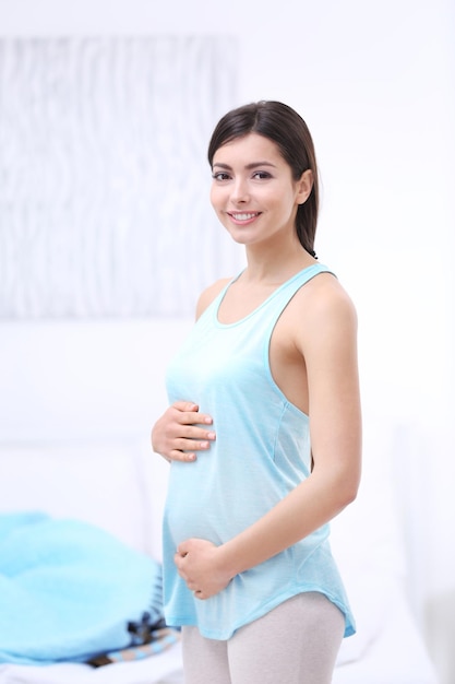 Portret pięknej szczęśliwej kobiety w ciąży dotykającej jej brzucha stojącego w jasnym pokoju