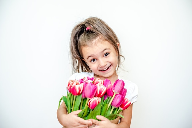 Portret pięknej uśmiechniętej dziewczynki z wiosennymi tulipanami na białym tle