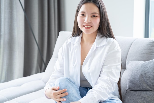 portret pięknej uśmiechniętej młodej azjatyckiej kobiety o długich ciemnych włosach w białej koszuli w nowoczesnym domu