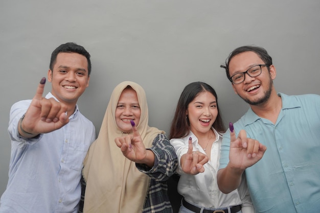 Portret podekscytowanej indonezyjskiej rodziny pokazujący mały palec zanurzony w fioletowym atramentu po głosowaniu na wybory powszechne lub Pemilu na prezydenta i rząd izolowane szare tło