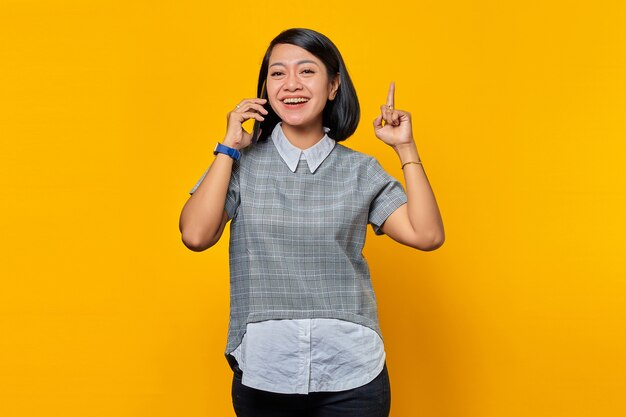 Portret podekscytowanej młodej azjatyckiej kobiety trzymającej smartfon z pomysłem lub pytaniem wskazującym palcem