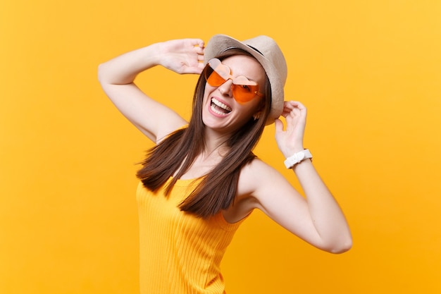 Portret podekscytowanej uśmiechniętej młodej kobiety w słomkowym letnim kapeluszu, pomarańczowe okulary położyć ręce na głowie, patrzeć na bok na białym tle na żółtym tle. Ludzie szczere emocje, koncepcja stylu życia. Powierzchnia reklamowa.