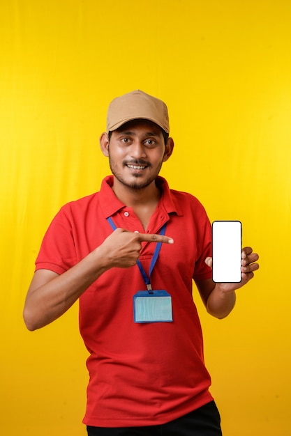 Portret podekscytowany szczęśliwy młody człowiek dostawy w czerwonej koszulce i pokazując smartphone na żółtym tle.