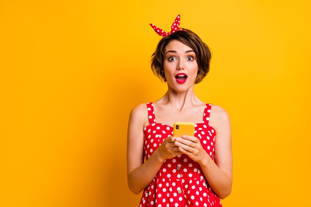 Portret podekscytowany zdziwiona dziewczyna korzysta z telefonu komórkowego uzyskaj niesamowite powiadomienie z sieci społecznościowej pod wrażeniem krzyk wow omg nosić czerwoną spódnicę w kropki retro izolowany jasny połysk kolor ściana