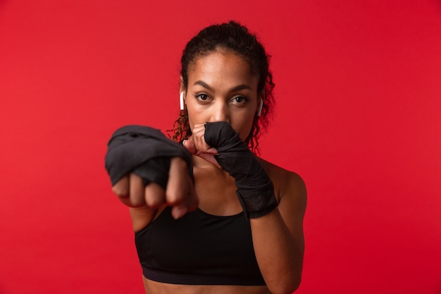 Portret Poważne Afroamerykanka W Czarnym Boksie Sportowym Z Bandażami Sportowymi Na Rękach, Odizolowane Na Czerwonej ścianie