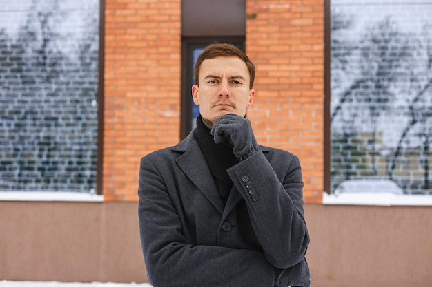 Portret poważnego męskiego przedsiębiorcy w zimowym płaszczu dotykającego podbródka i patrzącego w kamerę na ulicy