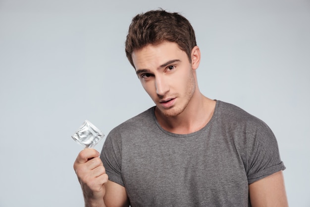 Zdjęcie portret poważnego mężczyzny trzymającego prezerwatywę na białym