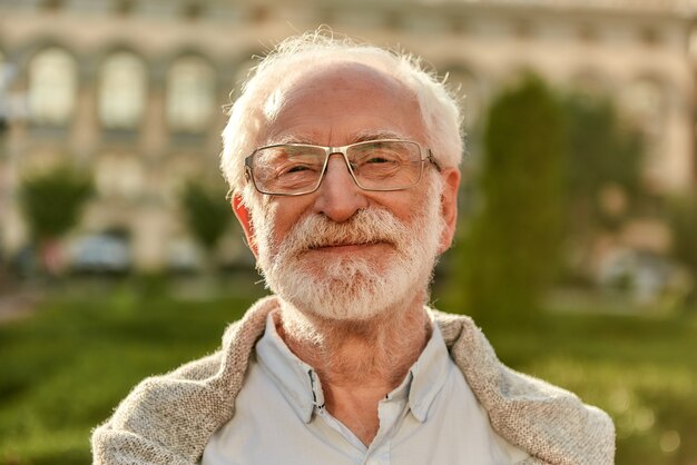 Portret pozytywnego nastawienia przystojnego, brodatego starszego mężczyzny w okularach, patrzącego na kamerę i uśmiechającego się