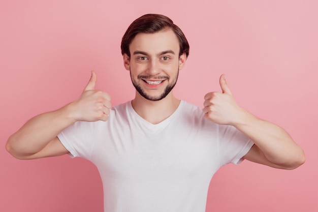 Portret pozytywnego wesołego faceta podniósł kciuk w górę ząbkującego błyszczącego uśmiechu na różowym tle
