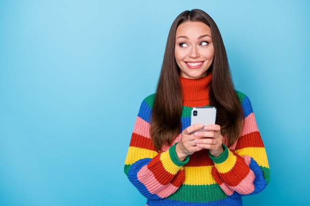 Portret pozytywnej wesołej dziewczyny używa smartfona wygląd copyspace post subskrybuj sprzedaż w mediach społecznościowych nosi sweter w stylu tęczy na białym tle nad niebieskim kolorem tła