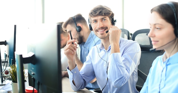 Portret pracownika call center w towarzystwie swojego zespołu. Uśmiechnięty operator obsługi klienta w pracy.