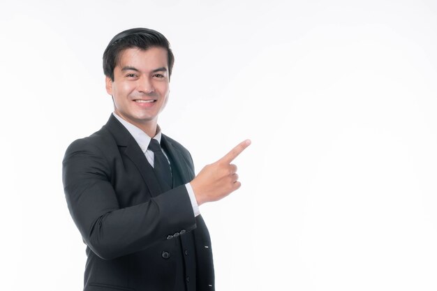 Portret pracujący azjatycki biznes człowiek ware garnitur ze szczęściem wskazującym palcem na puste miejsce, puste miejsce na reklamę lub produkt na białym tle - koncepcja biznesowa