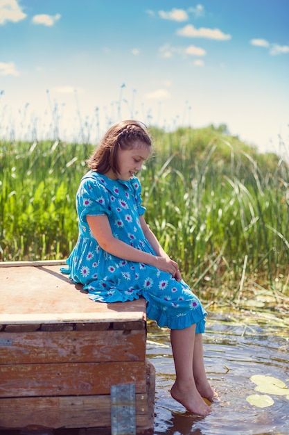 Portret pre-teen dziewczyna w niebieskiej sukience przed rzeką latem