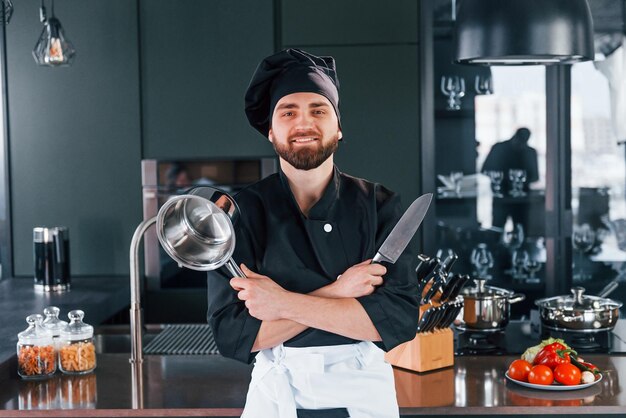 Portret profesjonalnego młodego kucharza w mundurze, który pozuje do kamery w kuchni